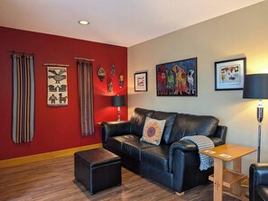 Un salon avec un mur rouge, un canapé en cuir noir, une table basse en bois et un lampadaire.