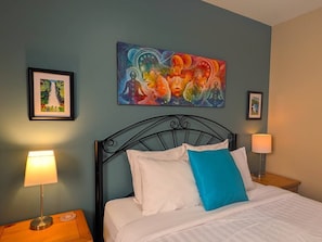 Ein Hotelzimmer mit einem Bett, zwei Nachttischlampen, einem gerahmten Kunstwerk über dem Bett und einem Wandbild zur Linken.