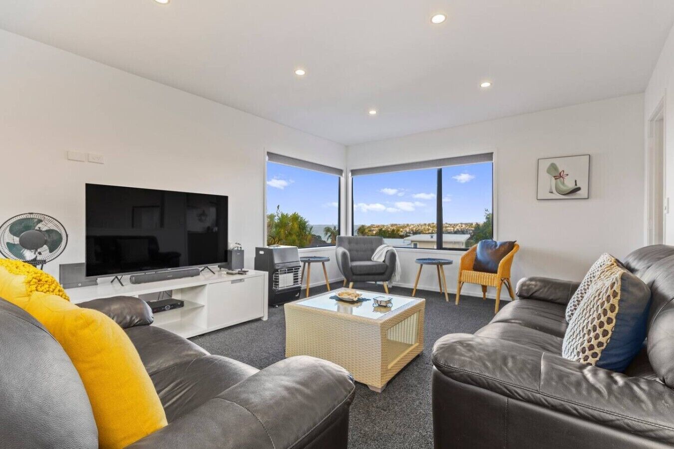 A modern living room with a flat-screen TV, leather sofas, a coffee table, and a balcony with a view.