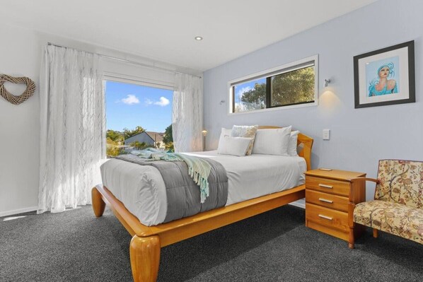 A bedroom with a bed, a nightstand, a chair, a window, and a painting on the wall.