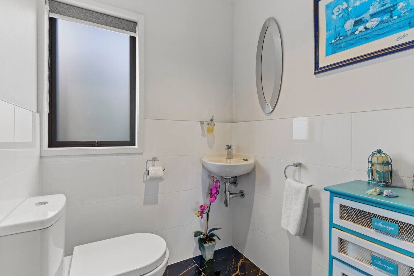 Un baño con inodoro, lavabo, espejo y un pequeño armario con una toalla.