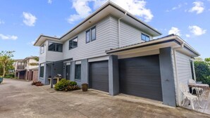 A two-story residential building with a garage, a covered driveway, and a small garden area.