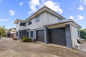 A two-story residential building with a garage, a covered driveway, and a small garden area.