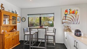A kitchen with a dining table, two chairs, a wooden cabinet, and a window with a view of trees.