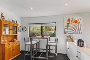 A kitchen with a dining table, two chairs, a wooden cabinet, and a window with a view of trees.