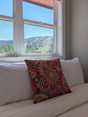 A white sofa with a colorful patterned pillow and a window with a view of greenery. - Kimberley Mountain Getaway | Ski, Golf & Adventure (Kimberley)