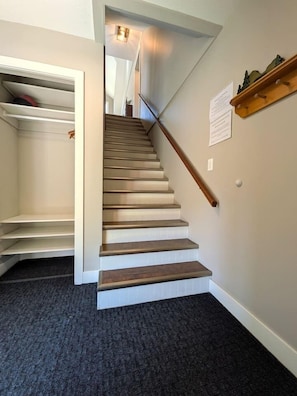 A staircase with wooden steps and a handrail, leading to a landing with a white closet and a shelf with decorative items. - Kimberley Mountain Getaway | Ski, Golf & Adventure (Kimberley)