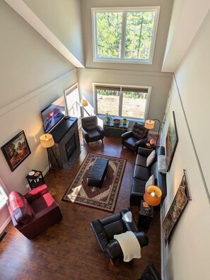 A spacious living room with a fireplace, leather sofas, and a large window offering a view of the outdoors. - Kimberley Mountain Getaway | Ski, Golf & Adventure (Kimberley)