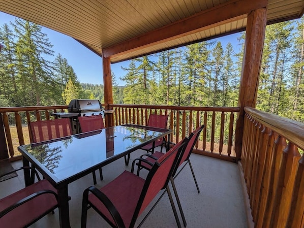 A covered outdoor deck with a glass-top table and chairs, surrounded by a wooden railing. - Kimberley Mountain Getaway | Ski, Golf & Adventure (Kimberley)