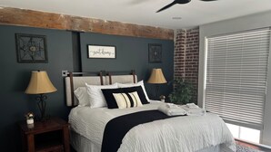 A bedroom with a bed, two bedside tables, a ceiling fan, a window with blinds, and a wall with a decorative sign. - Perfect 2-bedroom apartment near all attractions in downtown STL. Arch views! (St. Louis)