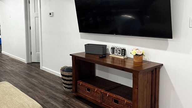 A living room with a flat-screen TV mounted on the wall, a wooden entertainment center below, a wicker basket, and a small table with a calendar. - Perfect 2-bedroom apartment near all attractions in downtown STL. Arch views! (St. Louis)