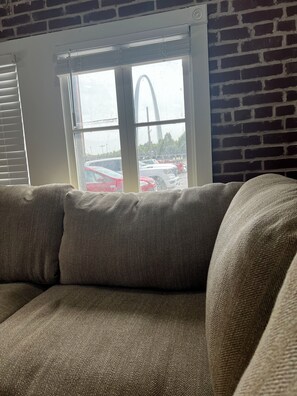 Ein Zimmer mit Backsteinwand, einem Fenster mit Jalousien und Blick auf einen Parkplatz mit Autos.