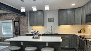 A modern kitchen with a central island, bar stools, pendant lighting, and a brick accent wall. - Perfect 2-bedroom apartment near all attractions in downtown STL. Arch views! (St. Louis)