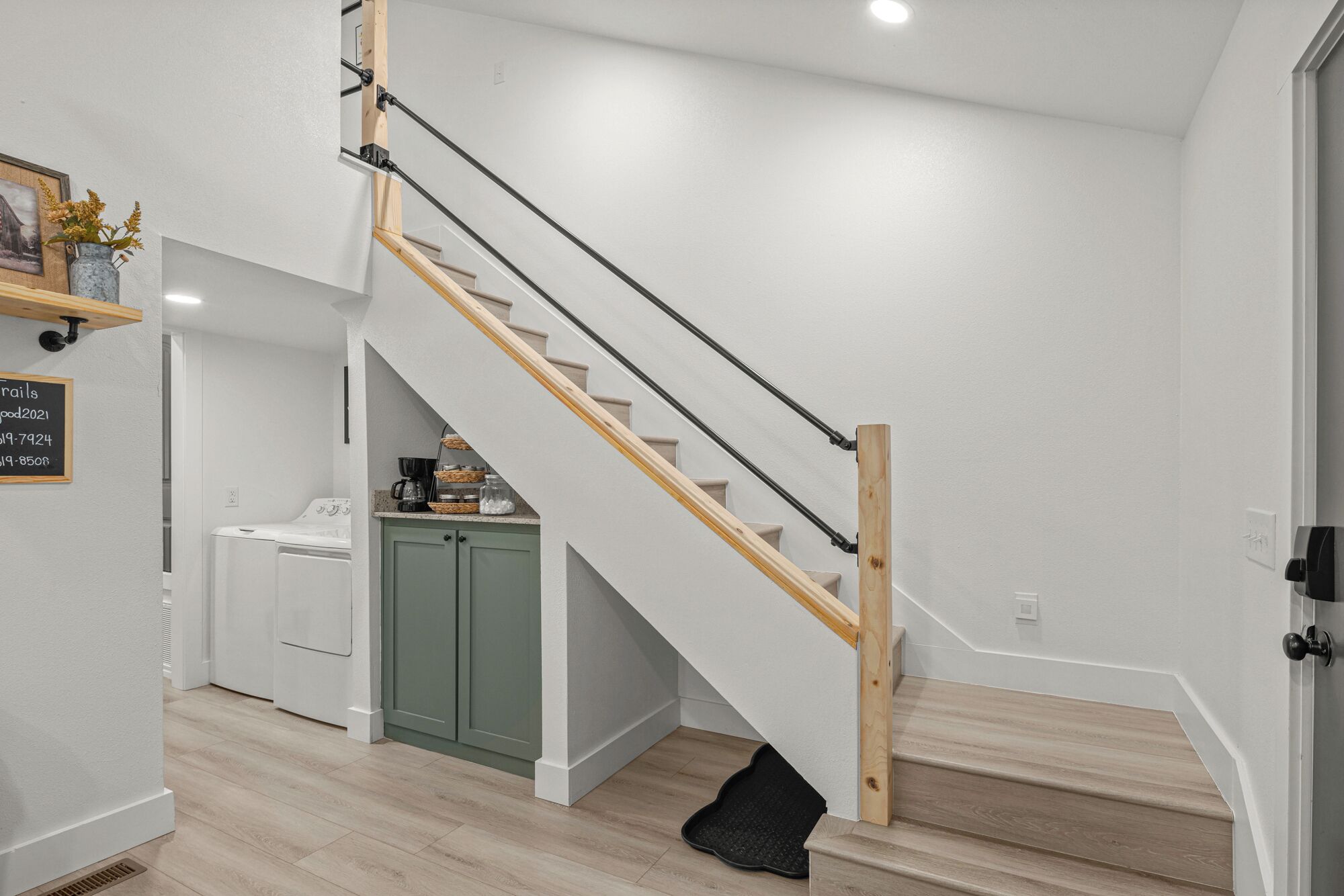 A staircase with wooden steps and black handrails, leading to a green cabinet and a white appliance.