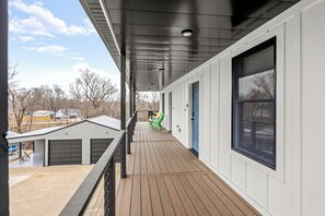 A covered porch with a wooden deck, a black railing, and a view of the neighborhood.