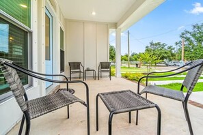 A covered outdoor seating area with wicker chairs and a table, overlooking a landscaped garden and street. - Searenity-Close to Downtown, Monthly`s Available (Pensacola)