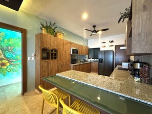 A modern kitchen with wooden cabinets, a central island, yellow chairs, and a ceiling fan. - 3-Bedroom Luxury Apartment, Beachfront in Progreso, Yucatán (Progreso)