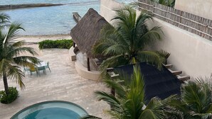 Zona de piscina amb vista al mar, una estructura amb teulada de palla i palmeres.