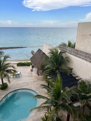A pool area with a view of the sea, a thatched-roof structure, and palm trees. - 3-Bedroom Luxury Apartment, Beachfront in Progreso, Yucatán (Progreso)