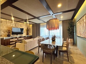 A modern living room with a flat-screen TV, a dining area with a glass table, and a large window with curtains. - 3-Bedroom Luxury Apartment, Beachfront in Progreso, Yucatán (Progreso)