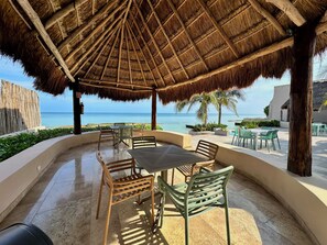 An outdoor seating area with a thatched roof, overlooking the sea.