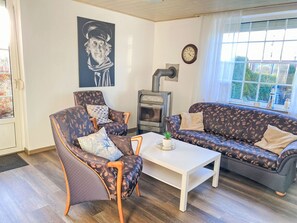 A living room with a sofa, armchair, and a table with a potted plant. A fireplace is visible in the background. - Sonnendeck by Interhome (Dornumersiel)