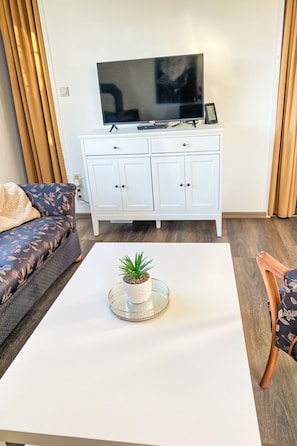 A living room with a white TV stand, a sofa, a coffee table with a plant, and a wooden chair. - Sonnendeck by Interhome (Dornumersiel)
