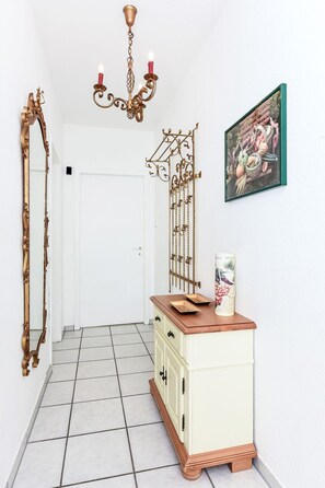 A hallway with a white door, a cream-colored cabinet with a wooden top, a wall-mounted picture frame, and a decorative metal rack. - Jupiter by Interhome (Dornumersiel)