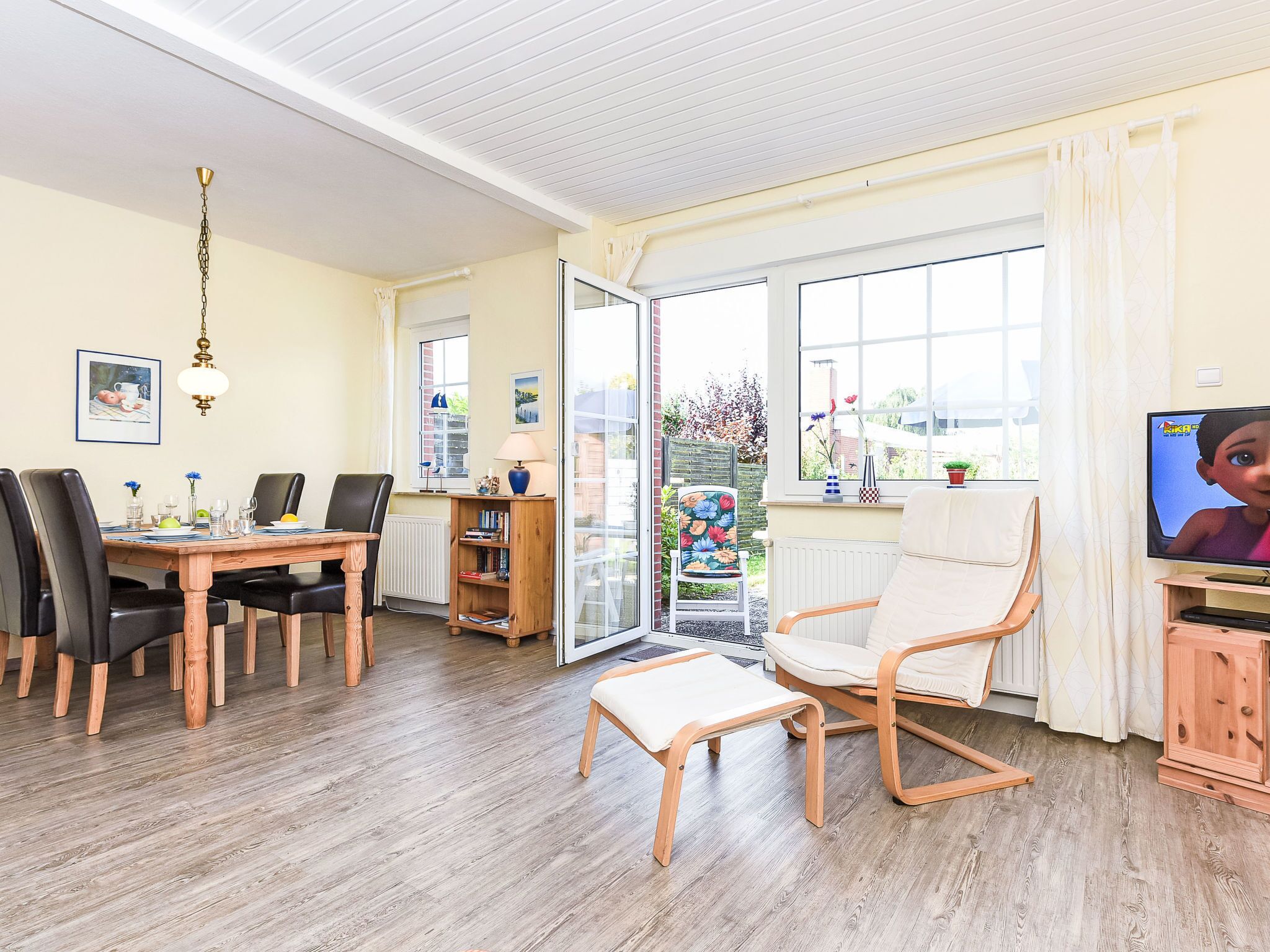 Un salon comprenant un coin repas, un téléviseur et donnant sur le jardin.