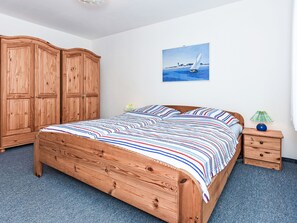 Ein Schlafzimmer mit einem hölzernen Bett, einem Nachttisch, einer Lampe, einem Kleiderschrank und einem Bild an der Wand.