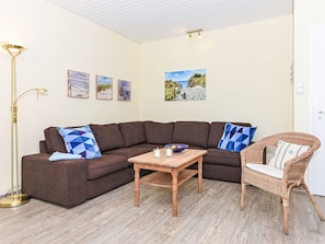 A living room with a brown sectional sofa, a wicker chair, a wooden coffee table, and wall art depicting coastal scenes. - Jupiter by Interhome (Dornumersiel)