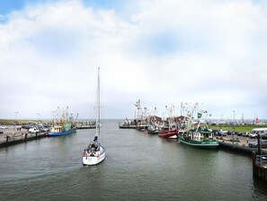 Ein Hafen mit mehreren vertäuten Booten, ein Segelboot im Vordergrund und ein Leuchtturm im Hintergrund.