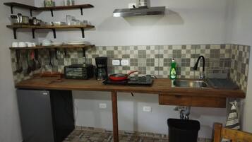 A compact kitchen with a built-in refrigerator, a coffee maker, a toaster, and a sink.