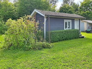 A small, single-story house with a tiled roof, surrounded by a well-maintained lawn and dense shrubbery. - Lötstugan by Interhome (Färjestaden)