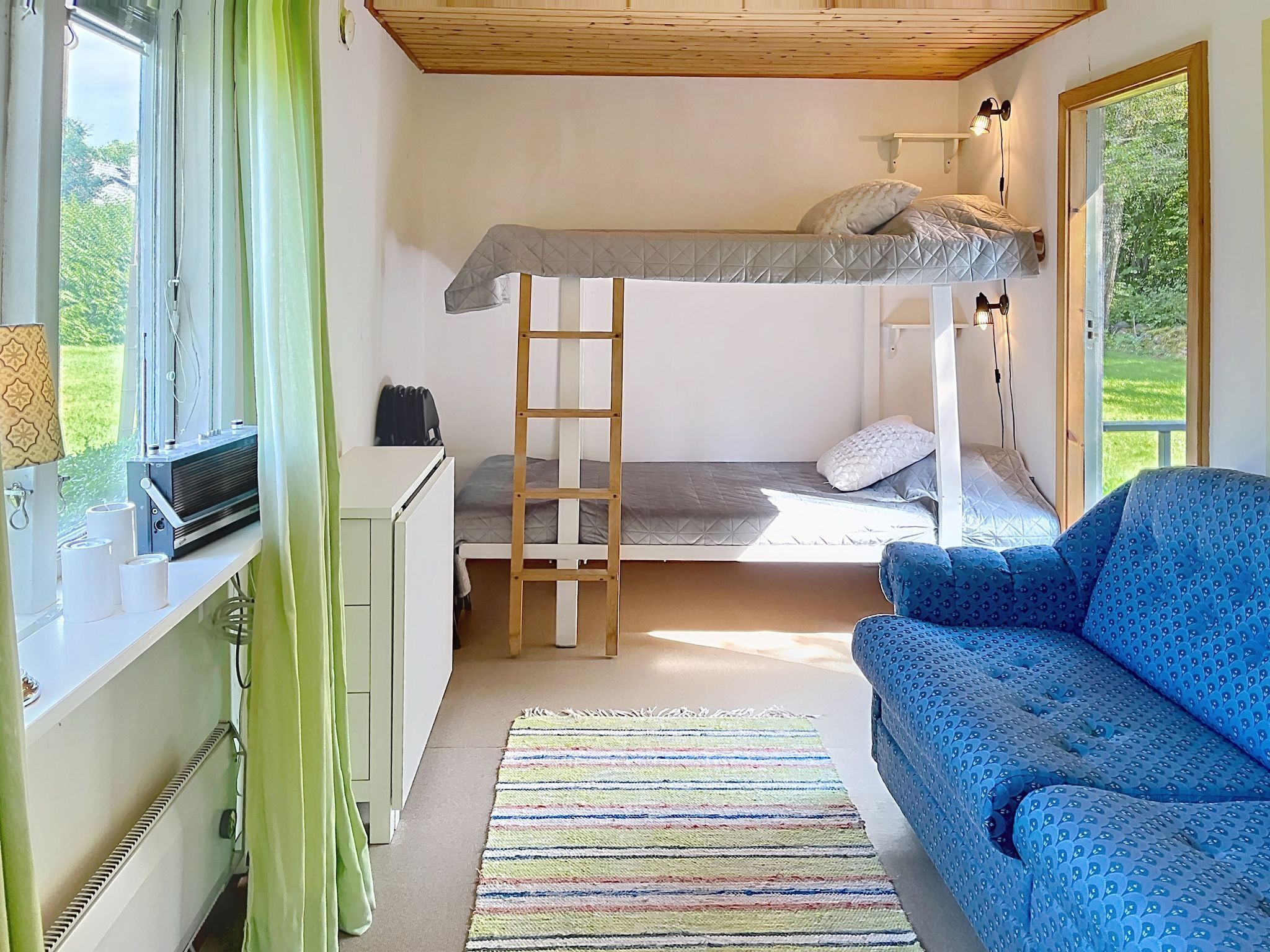 Habitación pequeña con una cama doble, un escritorio con ordenador, un sofá azul y vistas a zonas verdes.