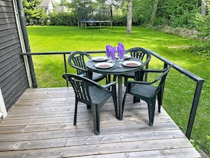 A wooden deck with a round table and chairs, a trampoline in the background, and a well-maintained lawn. - Lötstugan by Interhome (Färjestaden)