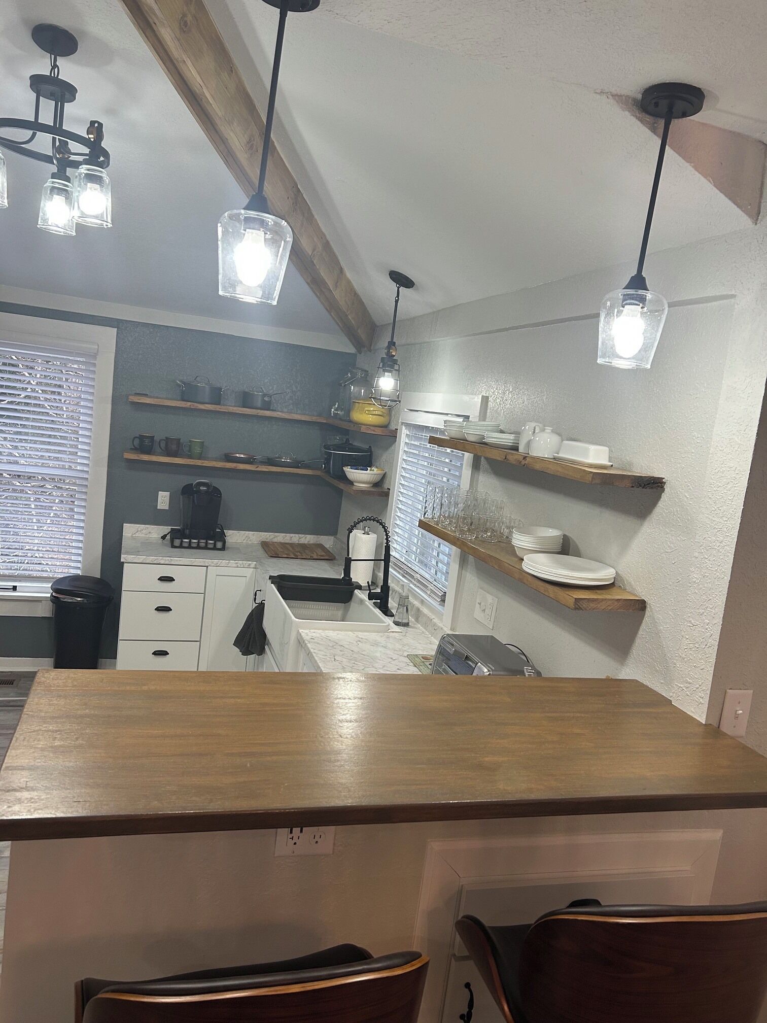 Uma cozinha com bancadas de madeira, luminárias pendentes e prateleiras com louças e utensílios de cozinha.
