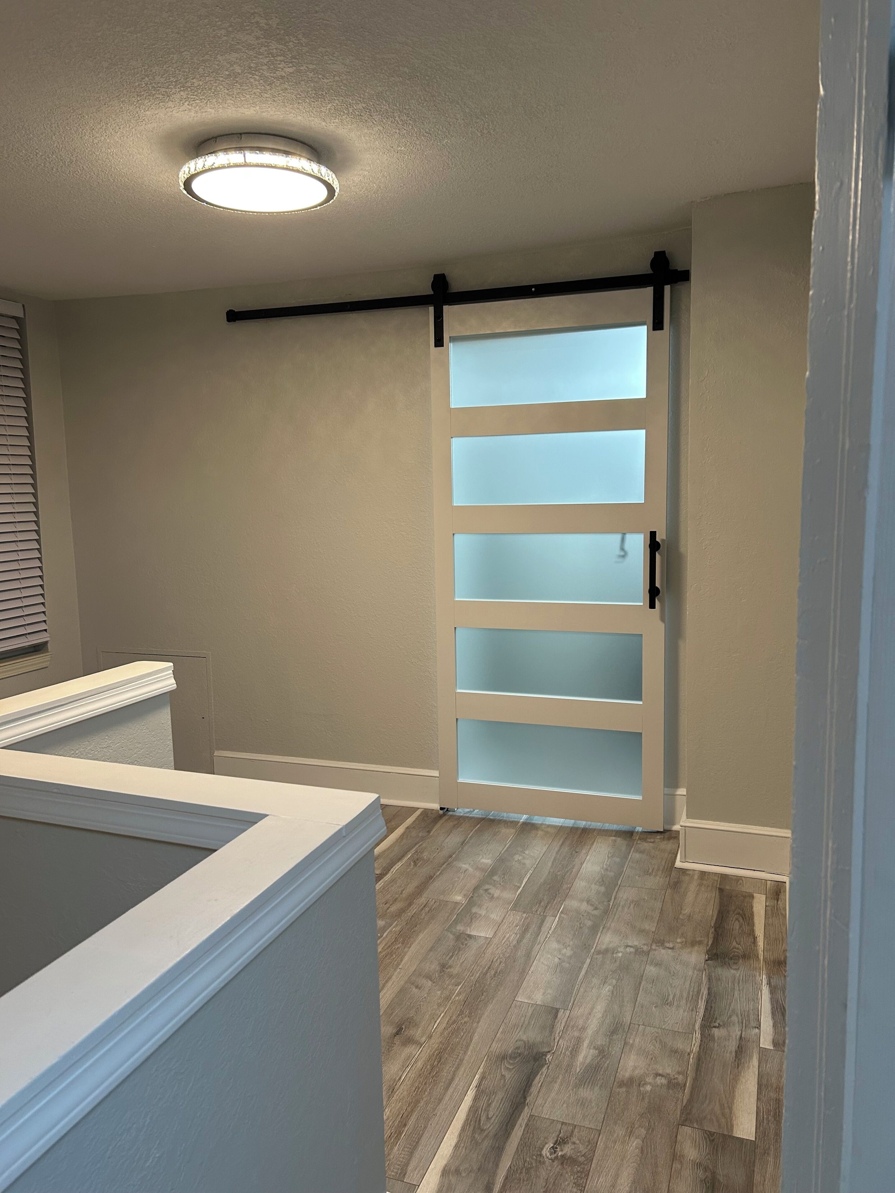 Un couloir doté d’une porte coulissante, d’un plancher en bois et d’un luminaire au plafond.