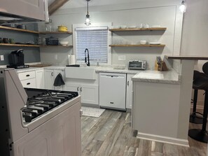 A modern kitchen with white cabinetry, a built-in stove, a window with blinds, and a countertop with a toaster and knives.