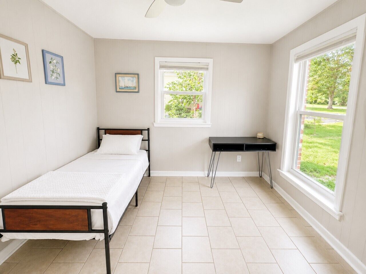 Un dormitorio con una cama individual, una mesita, una ventana y un ventilador de techo.