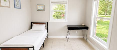 Un dormitorio con una cama individual, una mesita, una ventana y un ventilador de techo.