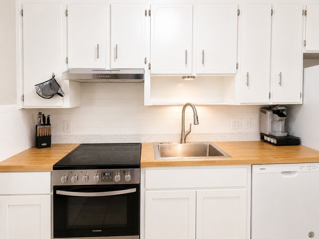 A kitchen with white cabinets, a black stove, a stainless steel sink, and a coffee maker.