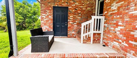 Fachada de ladrillo con puerta negra, barandilla blanca y asientos exteriores.