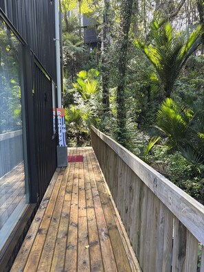 A wooden deck with a metal railing, surrounded by dense greenery and trees.