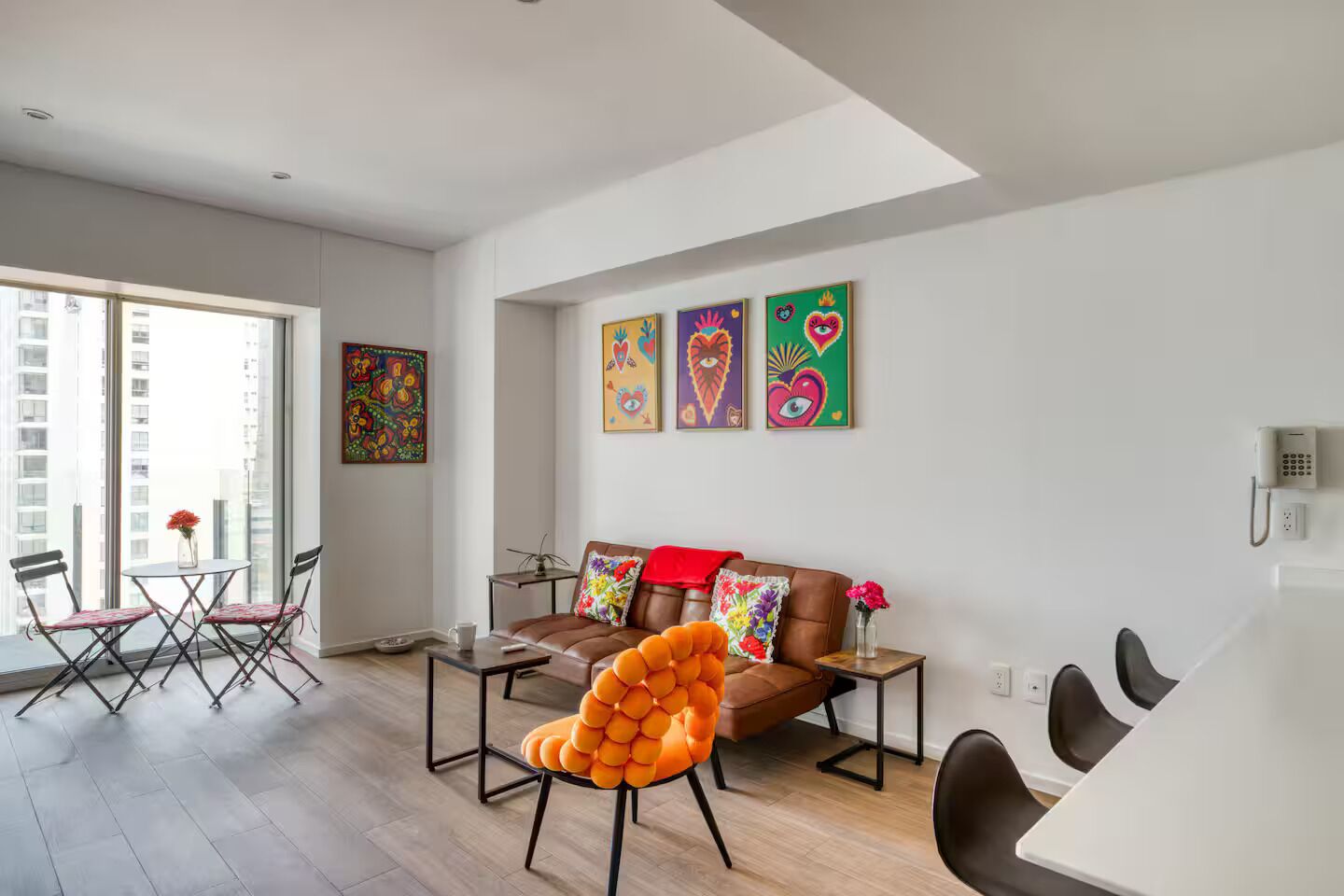 Una sala moderna con un sofá de cuero marrón, una silla naranja original y una zona de comedor con una mesa blanca.