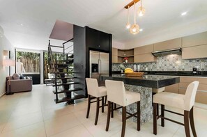 Une cuisine moderne dotée d’un îlot central, de tabourets de bar et d’un escalier avec un mur d’accent noir.