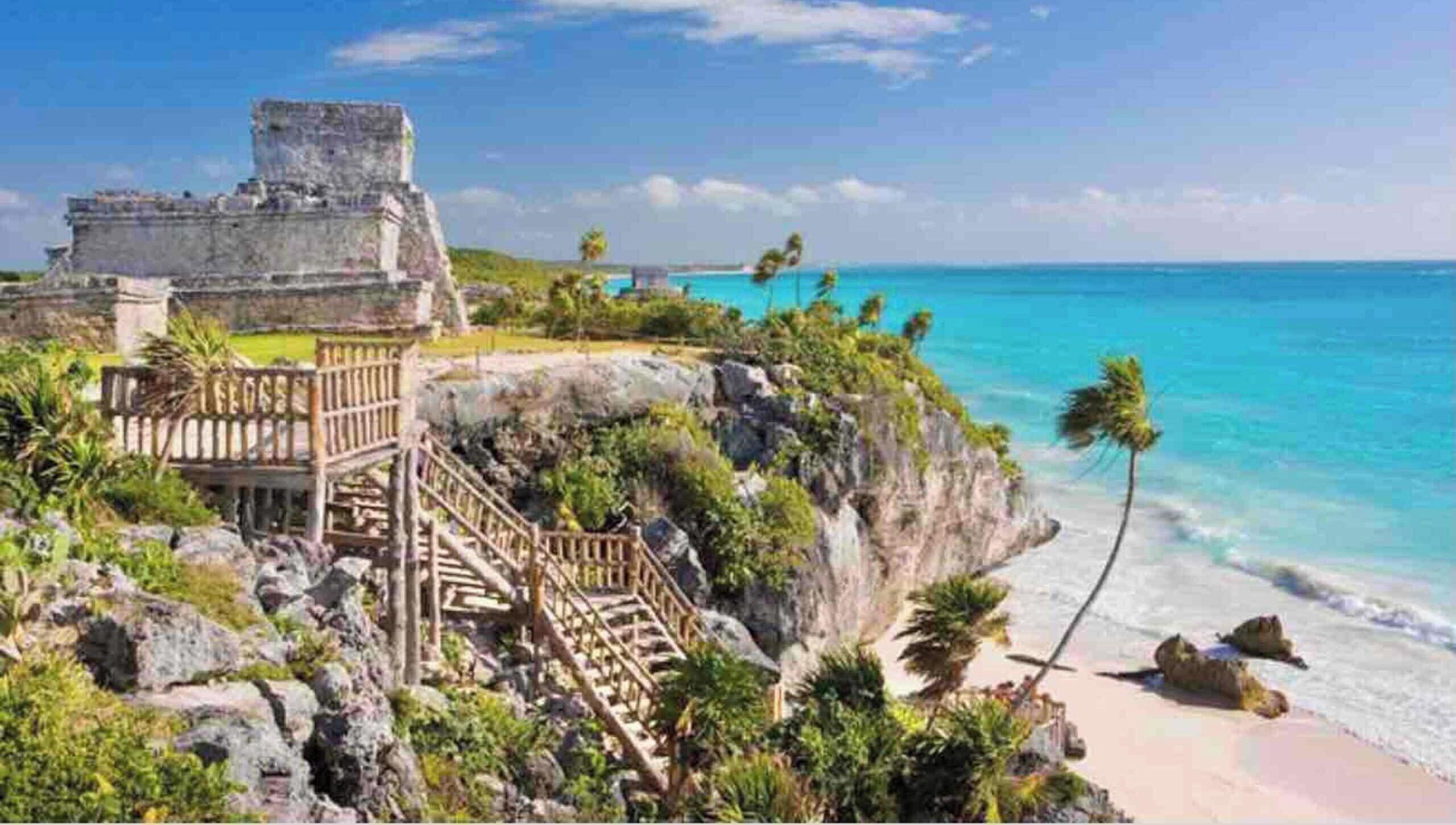Un site historique situé sur la côte, comprenant des ruines, un escalier en bois et une plage.