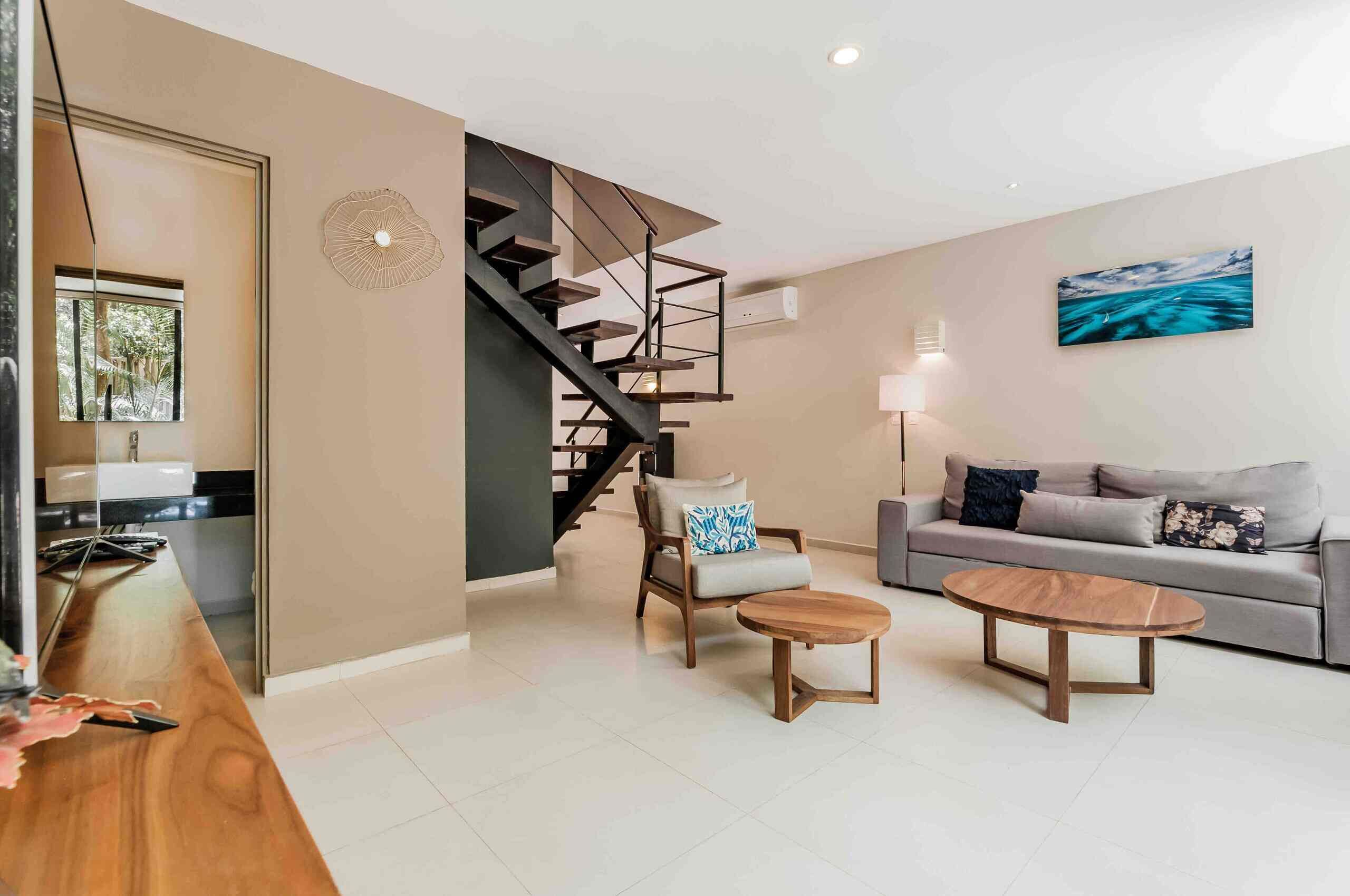 A modern living room with a staircase, a sofa, a coffee table, and a painting on the wall.
