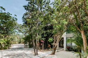 Un chemin pavé mène à un bâtiment portant le numéro « 2 », qui est entouré d’un feuillage dense et d’arbres.