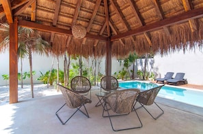 A covered outdoor seating area with a pool, surrounded by palm trees. - 3-bedroom townhome in lovely Tulum with AC and charm (Tulum)